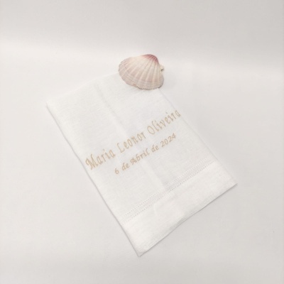 Toalha branca bordada com nome e data e concha em fundo branco