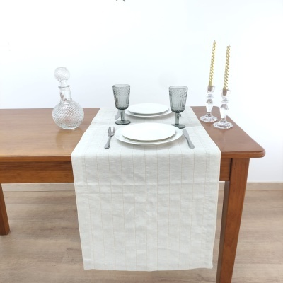 Mesa de madeira com toalha branca, pratos, taças cinzentas, garrafa de vidro e castiçais com velas