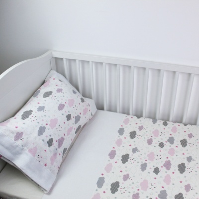 Berço branco com lençol e fronha com padrão de nuvens rosa e cinza