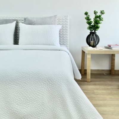 Cama com roupa de cama branca acolchoada perto de mesa de cabeceira com vaso e cortinados brancos