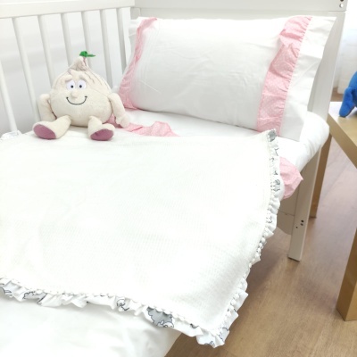 Cama pequena com roupa de cama branca e rosa e peluche em forma de alho sentado