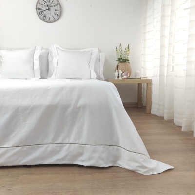 Cama com roupa de cama branca e almofadas, mesa de apoio e cortina branca em ambiente claro