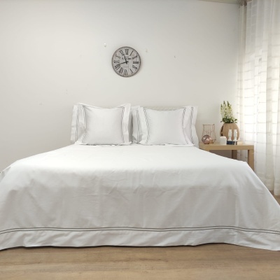 Cama de casal com colcha e almofadas brancas, relógio de parede e mesa lateral com decoração