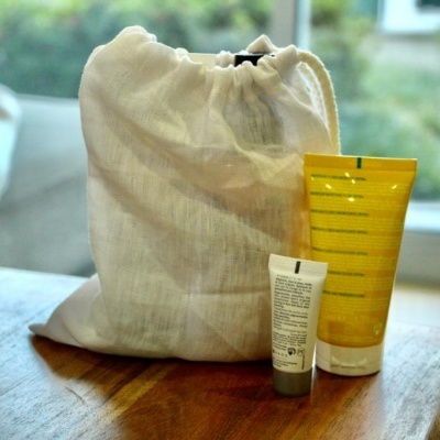 Dois tubos de cosméticos em frente a bolsa branca de tecido sobre mesa de madeira