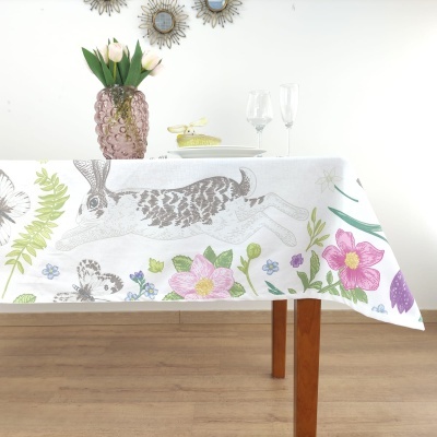Toalha de mesa branca com estampa de coelho e flores, vaso rosa com flores e duas taças em cima da mesa