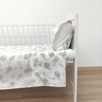Cama de bebé branca com roupa de cama decorada com balões cinza e bege.