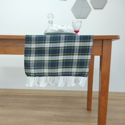 Mesa de madeira com toalha xadrez verde, branco, azul e preto com barra branca e um tabuleiro com frasco de vidro e copo