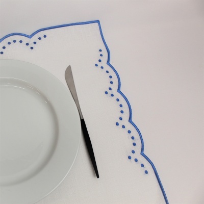 Toalha branca com bordado azul e prato branco com faca de cabo preto