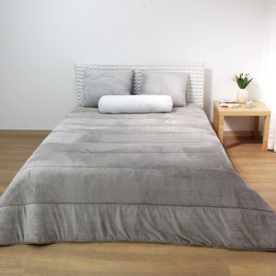 Cama de casal com roupa cinza e cabeceira branca trançada, mesa de cabeceira com flores, parede branca