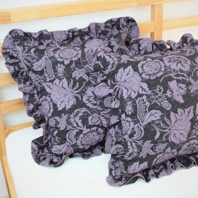 Par de almofadas decorativas roxo e preto com folhos numa cama de madeira