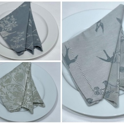 Três guardanapos de tecido com padrões decorativos em pratos brancos.