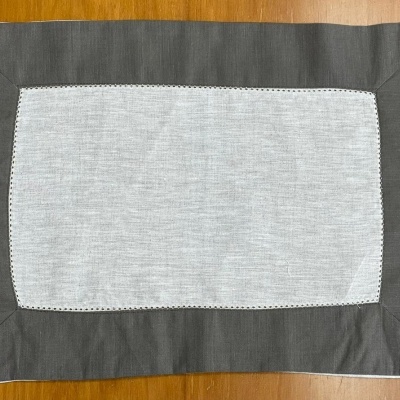 Toalha retangular cinza claro com borda cinza escuro sobre mesa de madeira