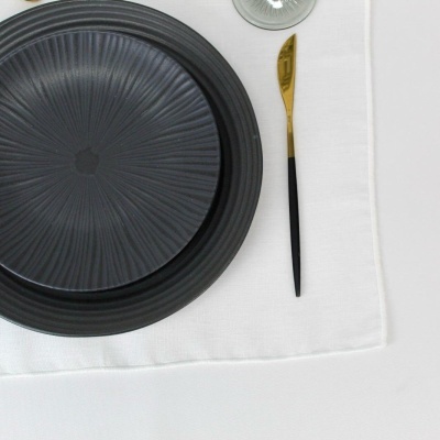 mesa posta com pratos pretos texturizados, guardanapo branco, copo transparente e talher preto e dourado