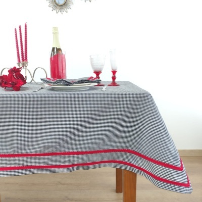 Mesa com toalha vichy preto e branco, copos e garrafa vermelha, velas vermelhas