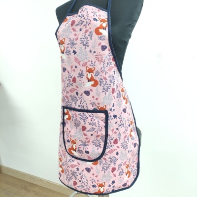 Avental rosa com padrão de raposas, flores e folhas, bolso preto, em manequim.