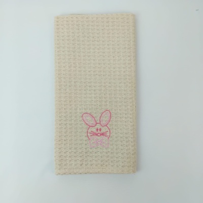 Toalha bege com textura quadriculada e bordado rosa de coelho