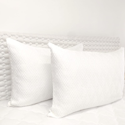 Par de almofadas brancas com padrão geométrico em relevo num ambiente branco