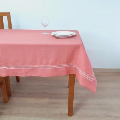 Toalha de mesa rosa com bordado branco sobre mesa de madeira com prato e copo