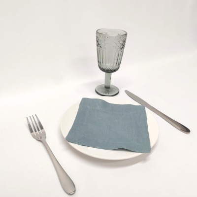 Conjunto de utensílios de jantar com prato branco, guardanapo azul, talheres prateados e copo de vidro