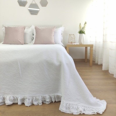 Cama com colcha branca e almofadas rosas e branca, mesa de madeira com vaso branco e flores, e três espelhos na parede