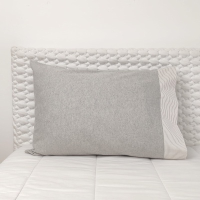 Travesseiro cinza com detalhe riscado branco sobre colchão branco e cabeça acolchoada