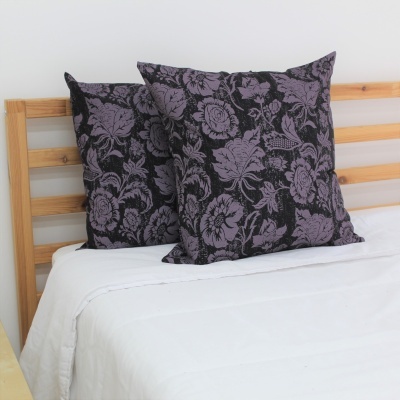 Almofadas pretas com padrão floral lilás sobre cama branca com cabeceira de madeira