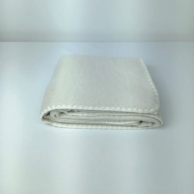 Manta branca dobrada com borda em renda sobre superfície branca