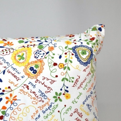 Almofada branca estampada com flores coloridas e texto manuscrito colorido