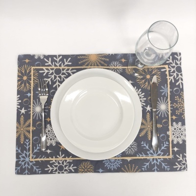 Conjunto de jantar com prato branco sobre suporte de mesa com flocos de neve e talheres ao lado