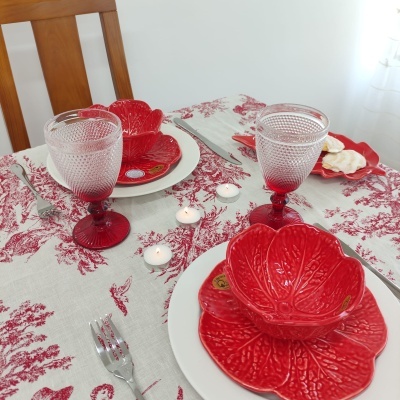 Conjunto de louça vermelha e taças de vidro sobre toalha branca com padrão vermelho numa mesa de madeira
