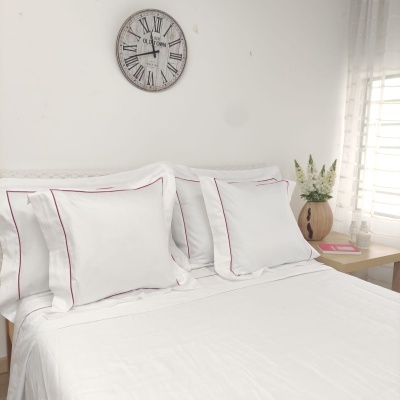 Roupa de cama branca com linhas vermelhas e relógio na parede