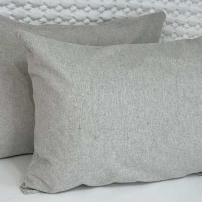 Duas almofadas retangulares cinzentas com textura suave sobre superfície clara e fundo branco texturizado