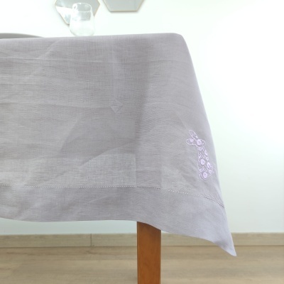 Toalha de mesa cinzenta com bordado roxo sobre mesa de madeira