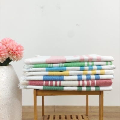 Mantass ou toalhas brancas listradas coloridas empilhadas sobre mesa de madeira com vaso branco e flores cor-de-rosa