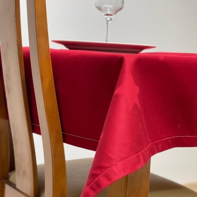 Mesa de madeira com toalha vermelha com padrão de estrelas, prato e taça com líquido vermelho.