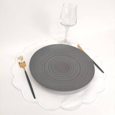 Conjunto de jantar com prato cinzento, talheres pretos e dourados, base branca e copo de vidro