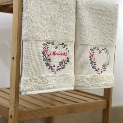 Duas toalhas brancas com bordado de coração floral penduradas numa estrutura de madeira