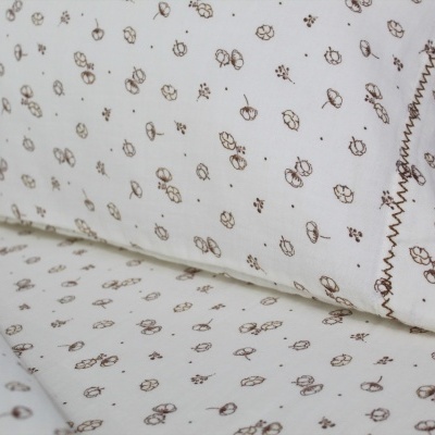 Fronha e lençol branco com padrão de pequenas folhas castanhas e bordado castanho na fronha