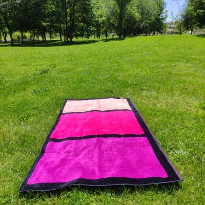 Tapete retangular rosa, fúcsia e pêssego com bordas pretas sobre relva verde num parque