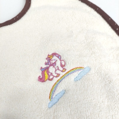 Babete creme com bordas castanhas e bordado de unicórnio e arco-íris