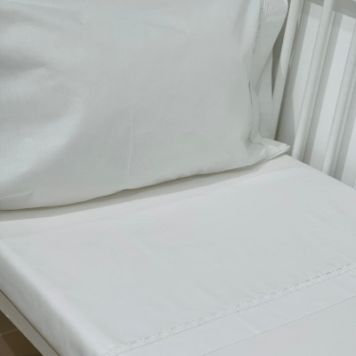 Conjunto de roupa de cama branco com almofada e lençol numa cama branca de madeira