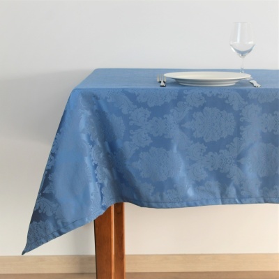 Mesa com toalha azul estampada floral, prato e talheres, copo de vidro