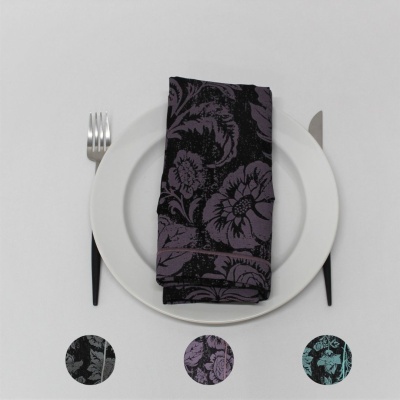 Guardanapo de tecido floral preto e roxo sobre prato branco com talheres.