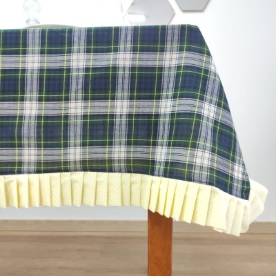 Toalha de mesa xadrez verde, azul e branco com barra amarela frisada, sobre mesa de madeira