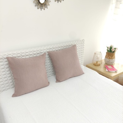 Cama branca com almofadas rosa claro e mesa de cabeceira com decoração