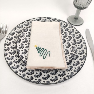 Conjunto de mesa com prato branco e preto, guardanapo branco bordado, talheres e copo de vidro cinzento