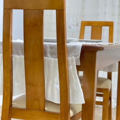 Mesa de madeira clara com toalha branca e cadeiras almofadadas creme