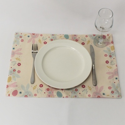 Jogo americano floral com prato branco, talheres metálicos e copo de vidro