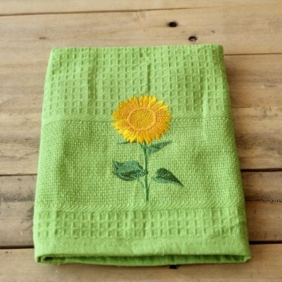 Toalha verde com bordado de girassol amarelo em superfície de madeira