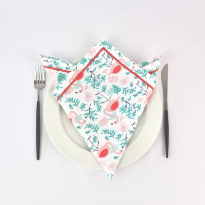 Guardanapo com padrão de aves cor de rosa e folhas verdes sobre prato branco com talheres